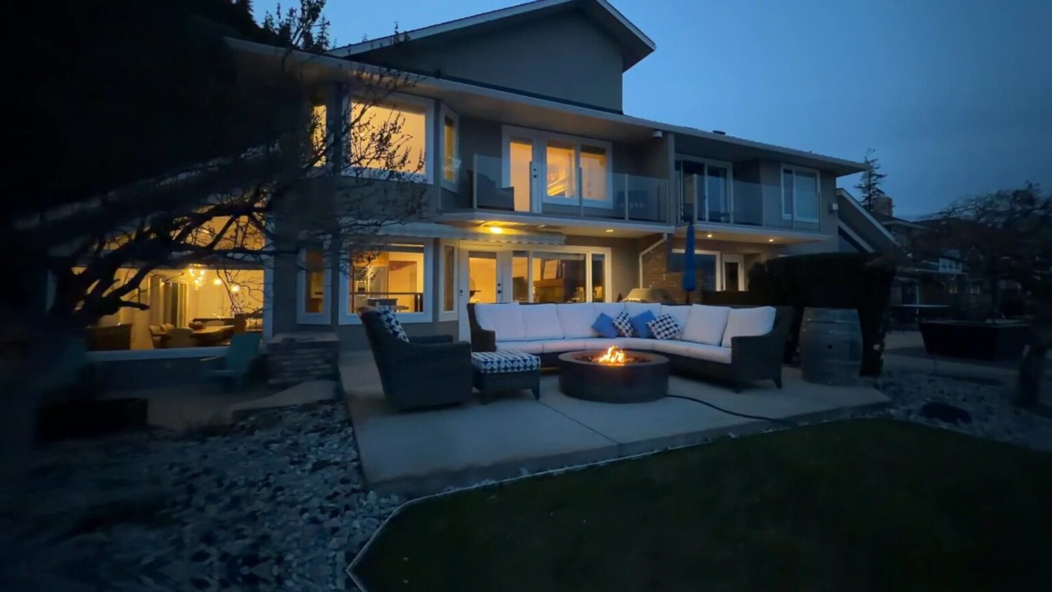 Frame from a cinematic walkthrough: West Kelowna home at dusk with the fire pit lit